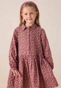 Robe pink imprimé léopard avec des manches longues, un col et un devant boutonné. Jupe évasée et un bandeau assorti complètent le look. Texture de tissu douce.