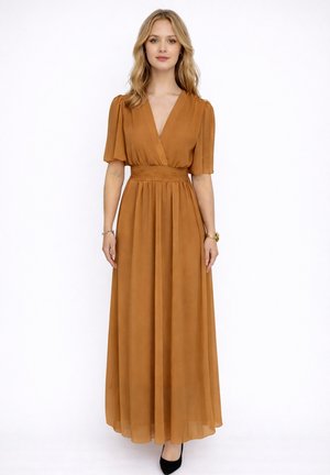 Vrouw draagt een vloerlang, roestkleurige jurk met korte mouwen en een aansluitende tailleband, staand tegen een witte achtergrond.