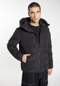 Sort pufferjakke med hætte, med kviltet tekstur, frontlynlås og sidelommer. Designet er enkelt og funktionelt.