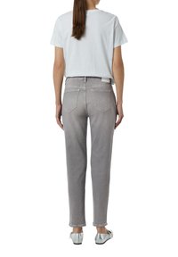 Lichtgrijze jeans met een rechte pijp, achterzakken en contrasterende stiksels, gecombineerd met een wit T-shirt en zilveren schoenen.