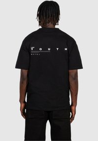 T-shirt en coton noir avec du texte blanc "LOST YOUTH" au dos. Manches courtes et coupe décontractée avec une texture lisse.