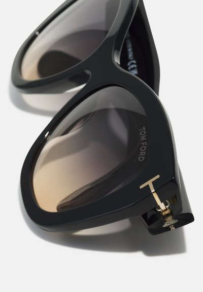Sunglasses med en svart plastram, gradient bruna linser och detaljer i guldton med "T"-logotypens accent på sidan.