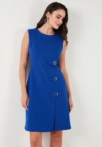 Blaues ärmelloses Kleid mit tailliertem Oberteil, A-Linien-Form und drei dekorativen Gürtelakzenten mit quadratischen Schnallen. Glatte Stoffstruktur.