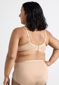 Reggiseno beige con spalline regolabili e chiusura a gancio, abbinato a un perizoma alto in vita coordinato. Tessuto morbido e design senza cuciture.