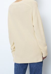 Pull en maille beige clair à coupe ample, avec des poignets et un ourlet côtelés, et un motif texturé. Porté avec un pantalon en denim bleu.