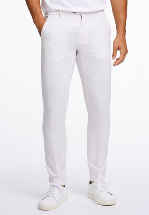Pantalon en lin blanc à coupe slim et texture subtile, doté de poches latérales et d'une fermeture éclair, associé à des baskets blanches.