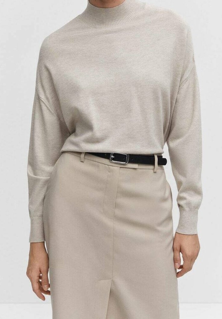 Pull en maille beige à col montant, épaules tombantes et manches longues, associé à une jupe taille haute beige clair et une ceinture noire.