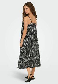 Rochie maxi cu un model alb-negru, cu bretele subțiri, având o croială lejeră și un material texturat. Este completată cu pantofi slingback negri, cu talpă plată.