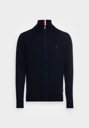 Marineblaue Strickjacke mit Reißverschluss und hohem Kragen, gerippten Bündchen und Saum, mit einem kleinen Logo in kontrastierenden Farben auf der Brust.