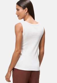 Top bianco senza maniche con un design a coste aderente, scollo rotondo e texture liscia; abbinato a pantaloni marrone scuro.