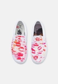 Chaussures blanches sans lacets présentant un design vibrant de motifs de lèvres roses et rouges. Les détails intérieurs incluent un message « L'amour c'est l'amour » et une doublure à motifs.