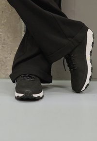 Černé sportovní boty s semišovou texturou, bílou mezipodešví a gumovou podešví, s černými tkaničkami a minimálními detaily.