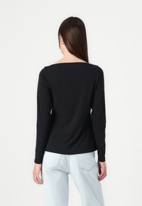 Black long-sleeve shirt with a square neckline, made from a smooth material, paired with light blue high-waisted jeans.