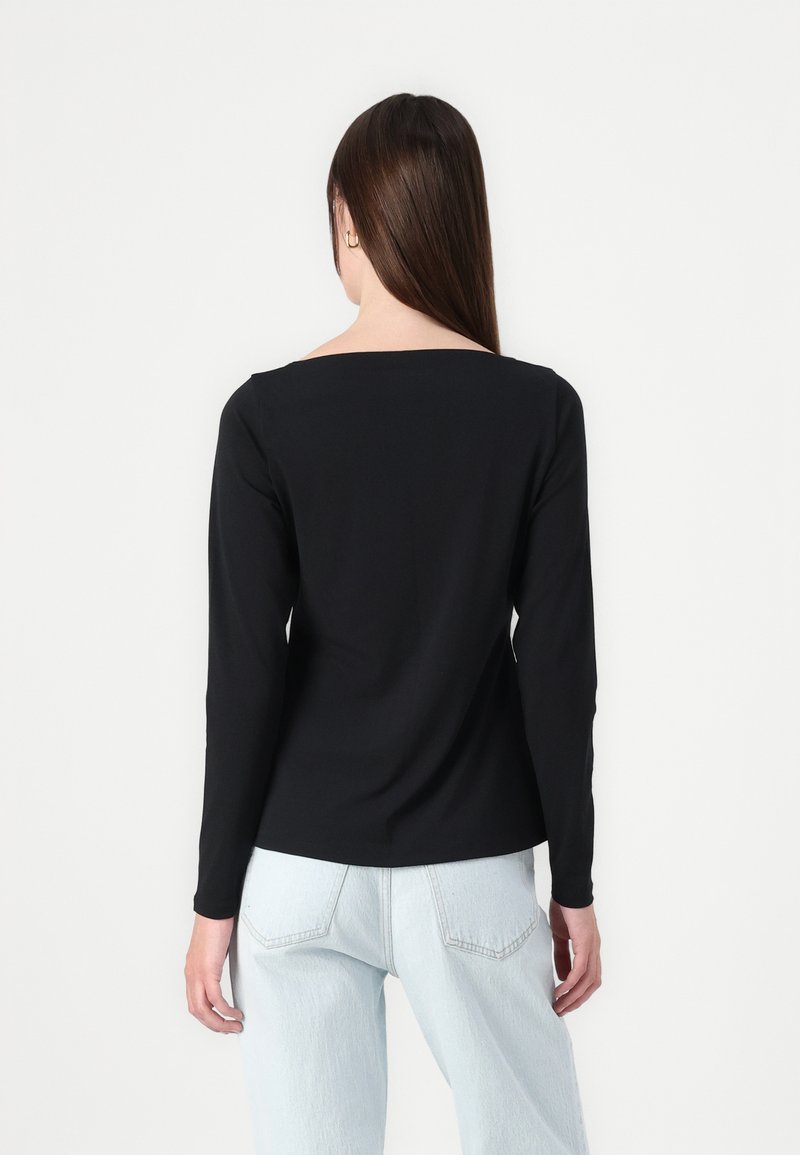 Schwarzes Langarmshirt mit quadratischem Ausschnitt, aus einem glatten Material, kombiniert mit hellblauen, hochtaillierten Jeans.
