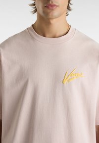 Helles rosa Baumwoll-T-Shirt mit Rundhalsausschnitt und kurzen Ärmeln. Mit einem gelben, gestickten "Vans"-Logo auf der linken Brust.