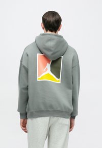 Γκρι φούτερ με κουκούλα σε άνετη γραμμή, με λευκό λογότυπο Jumpman σε πολύχρωμο τετράγωνο φόντο. Μαλακό ύφασμα με υφή.