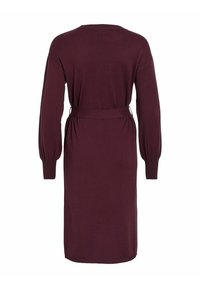 Vyno spalvos suknelė, pagaminta iš minkštos mezgimo medžiagos. Turi ilgas pūstuvas rankoves, juosmens raištį ir laisvą siluetą. Lygus paviršius ir kelio ilgio dizainas.