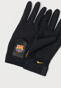 Mânuși negre cu un grip texturat pe degete, un logo Barcelona pe manșetă și branding galben Nike. Proiectate pentru căldură și flexibilitate.