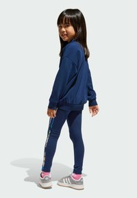 Meriino sveitslähtö, joka on yhdistetty sinisiin leggings-värisiin värikkäillä sivupaneeleilla. Vaaleanharmaat lenkkarit, joissa on valkoisia raitoja ja vaaleanpunaisia sukkia.