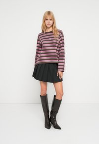 Ριγέ μπλούζα με μακριά μανίκια σε σκούρο καφέ με ροζ και λευκές ρίγες, συνδυασμένη με μαύρη φούστα με πιέτες και καφέ δερμάτινες μπότες μέχρι το γόνατο.