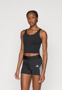 Μαύρο αθλητικό crop top και εφαρμοστά σορτς με ζώνη μέσης σε αντίθετο χρώμα. Τρεις λευκές ρίγες και λογότυπο στα σορτς. Λείο υφή.