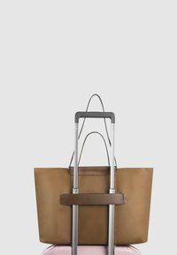 Braune synthetische Tragetasche mit zwei Griffen und einem horizontalen Riemen. Platziert auf einem pinkfarbenen Koffer mit einem eleganten silbernen Griff.