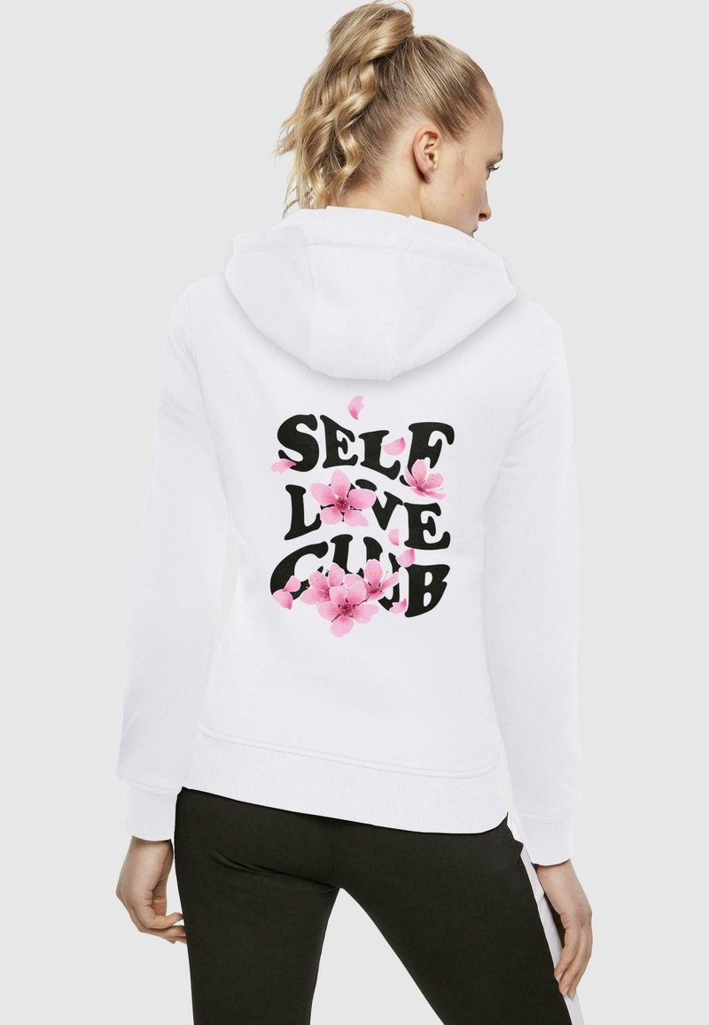 Felpa bianca con cappuccio e cordino, con la scritta "SELF LOVE CLUB" in bold nero e dettagli floreali rosa sul retro. Tessuto dalla texture liscia.