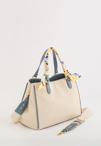 Bolso de lona beige con acentos en azul claro y herrajes dorados. Cuenta con dos asas superiores y una bufanda de patrón amarillo y azul atada en una de ellas.