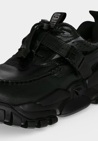 Μαύρο chunky αθλητικό παπούτσι με παχύ, υφασμάτινο πέλμα, ρυθμιζόμενο λουράκι με πόρπη και ελαστικό κλείσιμο με κορδόνι και σύρτη.