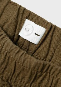 Verstelbare bruine stoffen tailleband met geplooide elastiek en witte knoopsgatachtig elastiek voor maatverstelling.