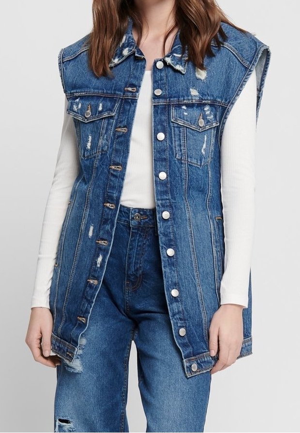 Jeansväst i ljusblå färg, med slitage, två bröstfickor och metallknappar. Lager på en vit långärmad topp.