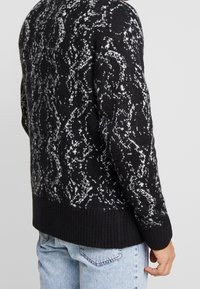 Sweter z dzianiny w czarno-białe wzory, z prążkowanym dołem, charakteryzujący się fakturowanym wzornictwem i luźnym krojem.