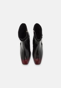Zwarte leren enkelboots met een glanzende afwerking, spitse neuzen en een rode verloopkleur aan de punten. Voorzien van een zijrits en zachte voering.