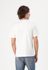 Hvit kortermet t-skjorte med rund hals laget av myk bomull, med en avslappet passform og rett kant, kombinert med blå denimjeans.