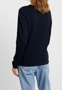 Granatowy sweter z długim rękawem, okrągłym dekoltem, ściągaczami i luźnym krojem, zestawiony z jasnoniebieskimi dżinsami z wysokim stanem.