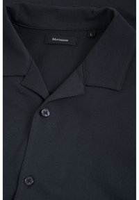 Polo noir en tissu doux, avec un col classique, une fermeture à un bouton, et une étiquette avec "Martinique" et la taille "L".