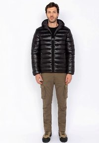 Czarna puchowa kurtka z zamkiem na przodzie, wysokim kołnierzem i kieszeniami po bokach; w zestawieniu z spodniami typu cargo. Kurtka posiada pikowany wzór i błyszczącą teksturę.