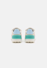 Zapatillas con parte superior beige, acentos azules en el collar y una media suela texturizada en color teal; con punta redonda y talón acolchado.
