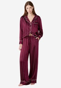 Burgundy randiga pyjamas-set i mjukt tyg som har en knäppning upptill med en ficka och löstsittande byxor med resårmidja.