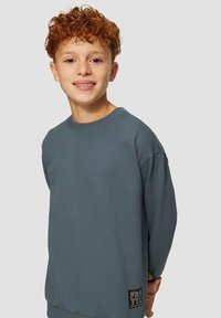 Grijze sweatshirt met lange mouwen van zachte stof, voorzien van een ronde hals en een logotag aan de zoom. Casual ontwerp met verlaagde schouderranden.