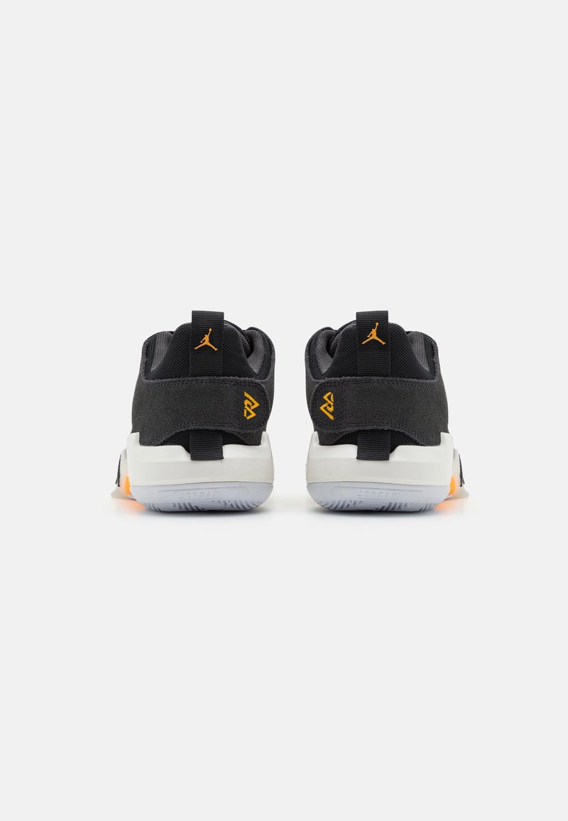 Zapatillas deportivas negras con parte superior de ante y malla, acentos naranjas, cuello acolchado, suela de goma plana y tiradores traseros para facilitar su puesta.
