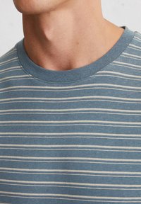 T-shirt bleu à rayures avec un col rond, doté de fines rayures blanches sur un tissu texturé, montrant un gros plan du col et de la partie supérieure de la poitrine.