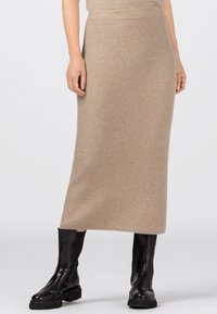 Beige knit midi kjol med vertikalt ribbmönster; i kombination med svarta glansiga anklandsskor. Texturerad tyg och figurnära siluett.