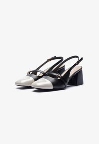 Tacchi slingback in pelle nera con punta a punta bianca lucida. Presentano un tacco a blocco e doppie cinghie con dettagli in metallo dorato.