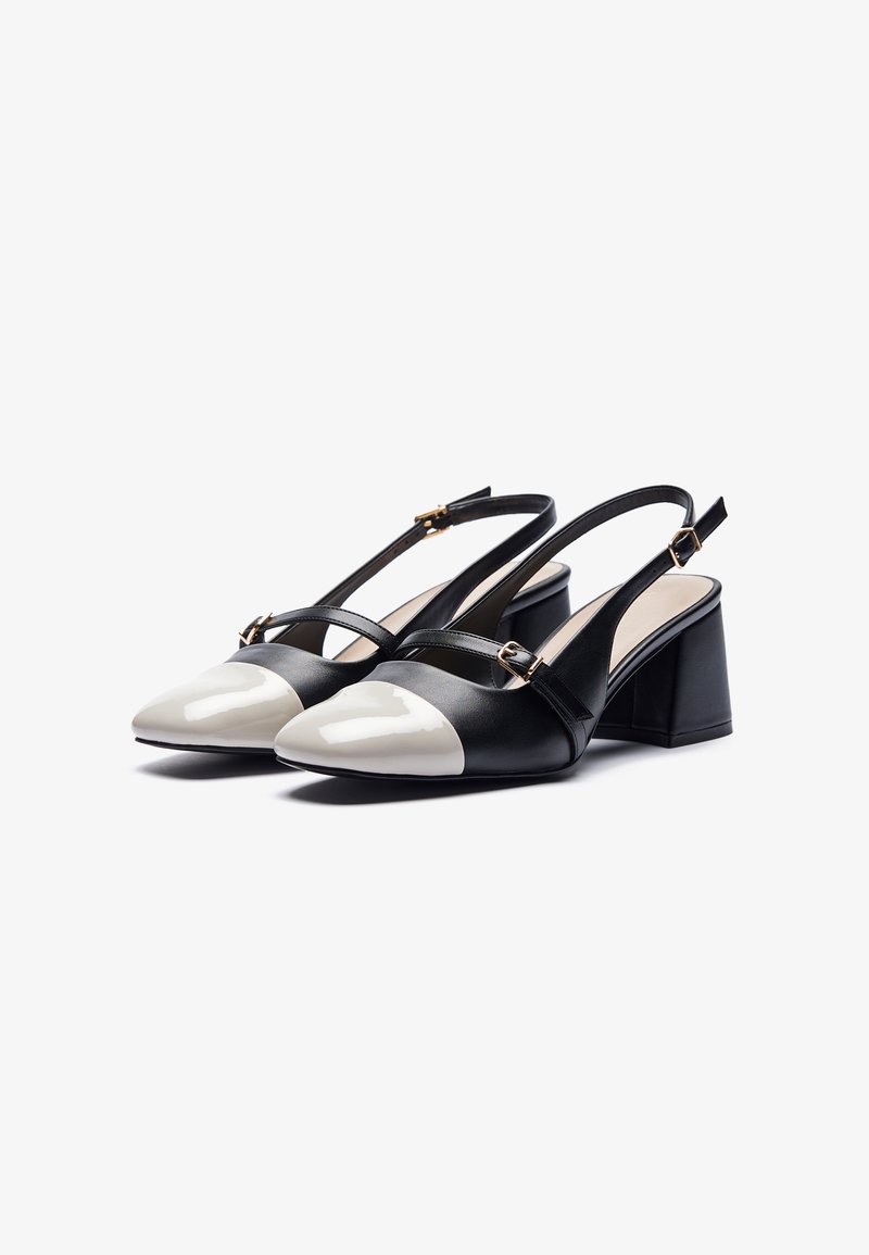 Talons slingback en cuir noir avec un bout pointu blanc brillant. Dispose d'un talon bloc et de doubles sangles avec des accents en matériel doré.