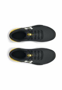 Une paire de chaussures de sport noires et jaunes avec des semelles blanches, un logo Under Armour blanc, des lacets noirs et une tige en maille, vue de dessus.
