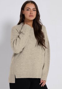 Maglione lavorato a maglia color beige chiaro con una vestibilità rilassata, polsini a coste e spacco sui lati. Tessuto morbido, scollatura rotonda e maniche lunghe.