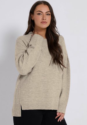 Pull en tricot beige clair avec une coupe décontractée, des poignets côtelés et des fentes sur les côtés. Texture douce, col rond et manches longues.