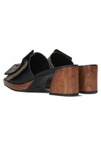 Zwarte leren sandalen met een geweven accent, open achterkant en een gebogen houten blokhak. Gestructureerde banden met een grote strikdetail.