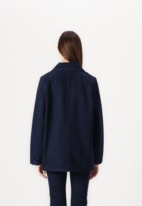 Veste en denim bleu foncé avec un col classique, une coupe décontractée et des manches longues. Caractéristiques : coutures visibles et texture lisse.